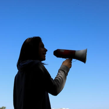 A silhouette of a woman with a microphone against a blue sky