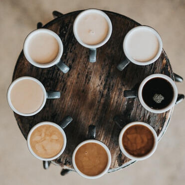 Cups of tea with varying degrees of milk arranged in a circle on a wooden stool. The milk produces different shades of browns